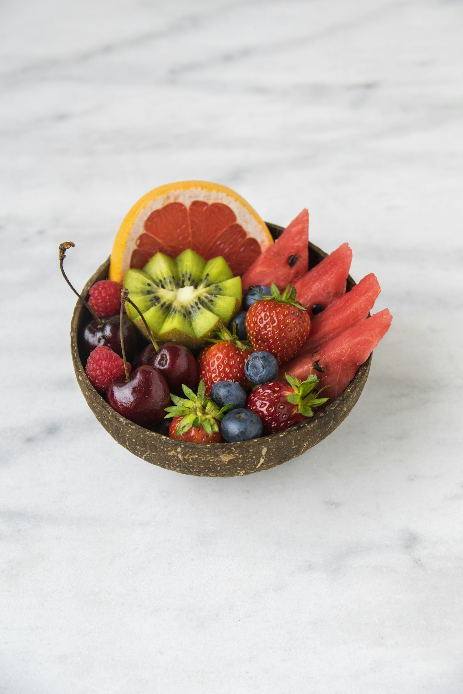 A bowl of fresh cut fruit including watermelon, kiwi, berries, and citrus